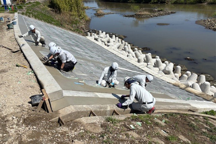 複数の作業服の人物が川の近くで工事を行っている様子