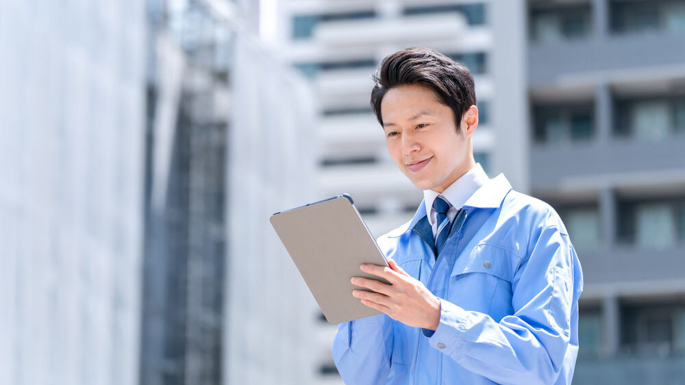 タブレットを操作する青い作業服を着た男性の写真